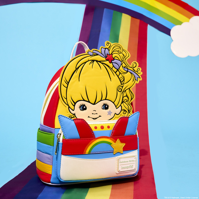 Rainbow Brite cosplay mini backpack featuring Rainbow Brite in appliqué detail and her rainbow outfit on the front and side pockets. Bag sits against a blue background with a rainbow on it.